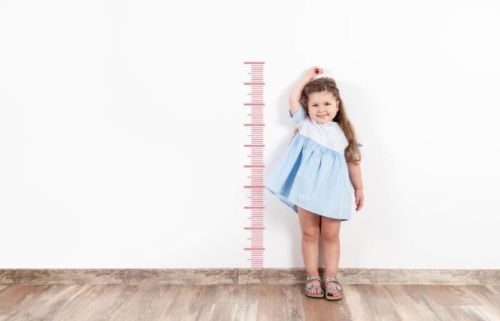 فتاة صغيرة تقف بجانب مقياس الطول المرسوم على الحائط وتضع يدها فوق رأسها