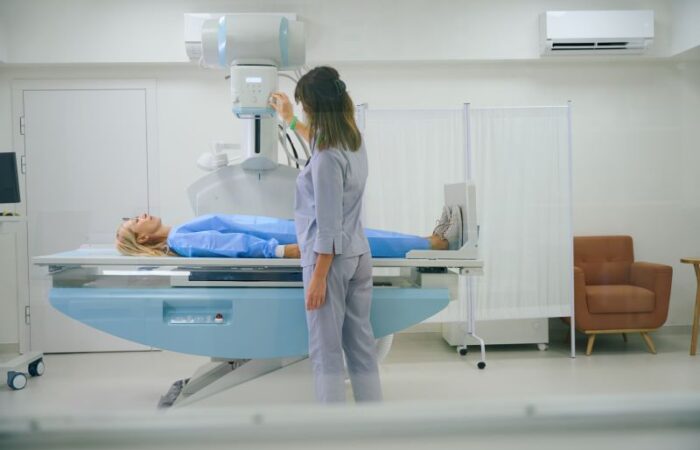 امرأة مستلقية على سرير جهاز طبي وفوقه جهاز إشعاعي