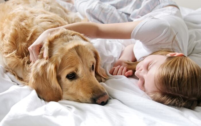 بنت شعرها أشقر ممددة على السرير وبجانبها كلب بني اللون