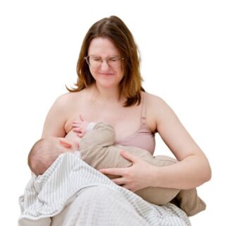 أم تقوم بإرضاع طفلها الرضيع وهي جالسة وتظهر علامات الألم في تعبيرات وجهها