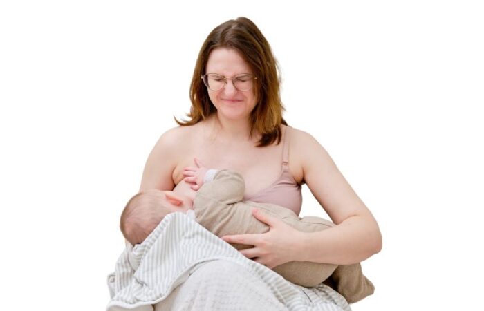 أم تقوم بإرضاع طفلها الرضيع وهي جالسة وتظهر علامات الألم في تعبيرات وجهها