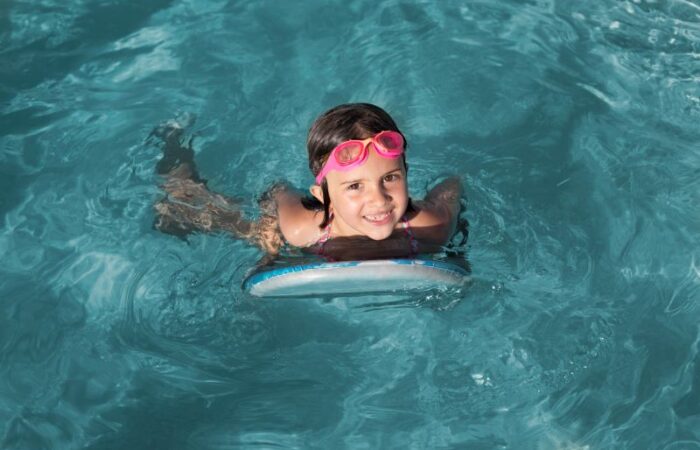 بنت مبتسمة ترتدي نظارات مخصصة للسباحة متواجدة ضمن الماء