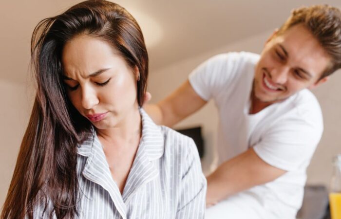 رجل مبتسم يضع يده على كتف امرأة حزينة مغمضة العينين تجلس على السرير وتظهر على وجهها علامات الإشمئزاز