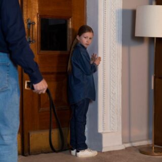 رجل بالغ يمسك بيده حزام البنطال وتقف أمامه بنت تقف خائفة بجانب الباب