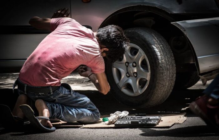 صبي يلبس ثياب مُتسخة وممزقة يقوم بإصلاح عجلة السيارة