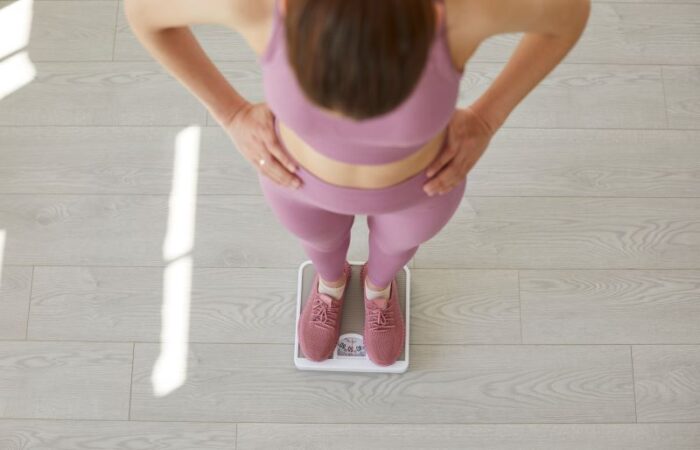 امرأة بالغة تضع يديها على خصرها وهي تقف على ميزان الوزن