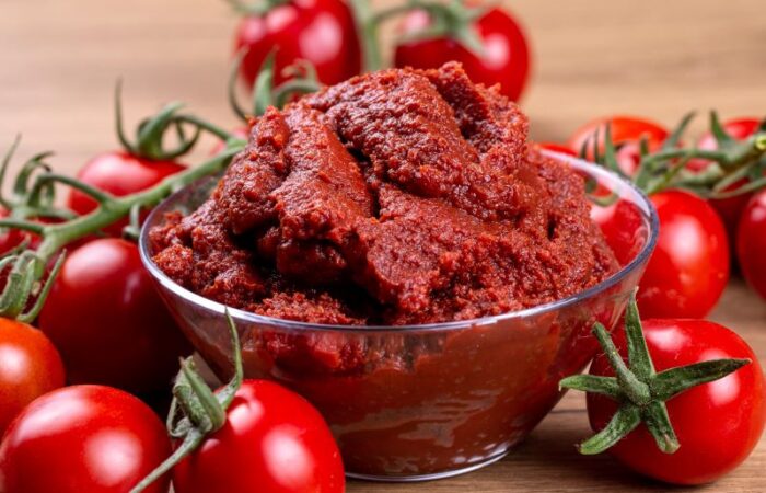 ثمرات طماطم يتوسطها صحن زجاجي شفاف ممتلئ بمعجون البندورة