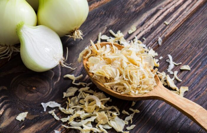 قطع من البصل وبجانبهم ملعقة خشبية تحتوي على شرائح البصل المجفف