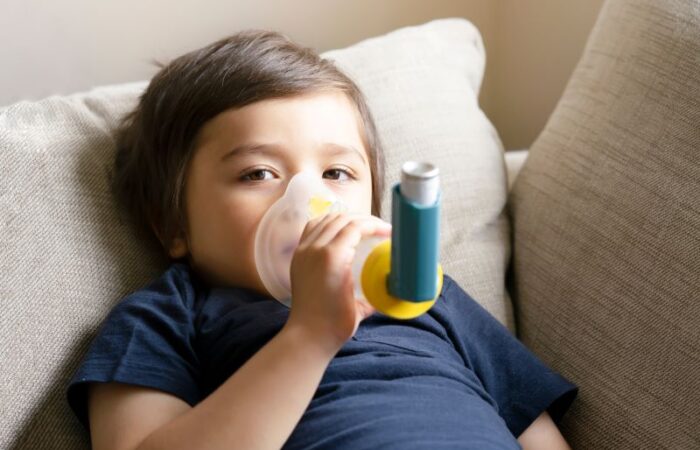 صبي مستلقي على الأريكة ويمسك بقناع بخاخ يحتوي على دواء للربو ويضعه على أنفه وفمه