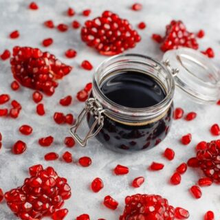 قطرميز زجاجي يحتوي على سائل أسود اللون وحوله قطع وحبات من الرمان