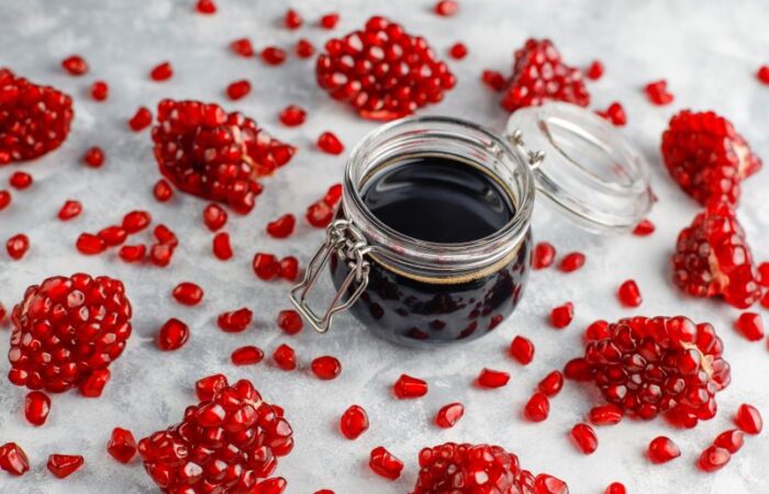 قطرميز زجاجي يحتوي على سائل أسود اللون وحوله قطع وحبات من الرمان