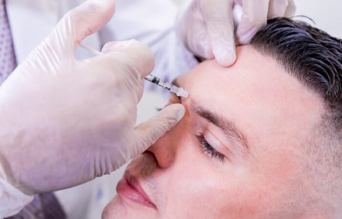 يدي طبيب يرتدي قفازات يحقن جبين شخص بالغ مستلقي بمادة البوتوكس