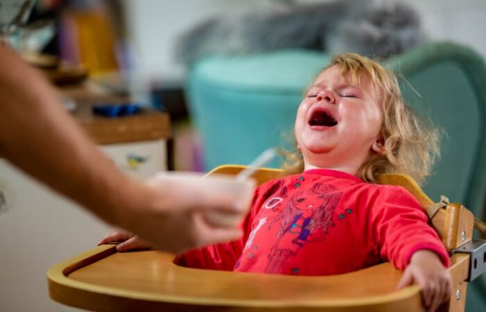 فتاة شعرها أشقر تجلس على كرسي الطعام المخصص للأطفال وهي تبكي