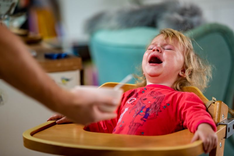 فتاة شعرها أشقر تجلس على كرسي الطعام المخصص للأطفال وهي تبكي