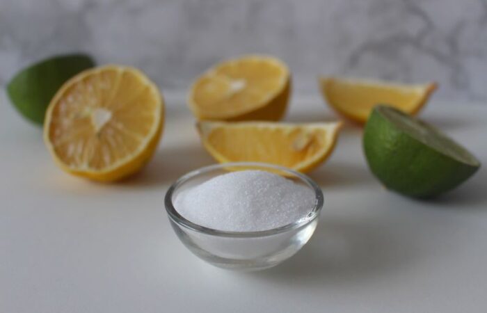 صحن زجاجي شفاف مملوء بحبيبات بيضاء اللون وحوله قطع من الليمون الحامض والبرتقال