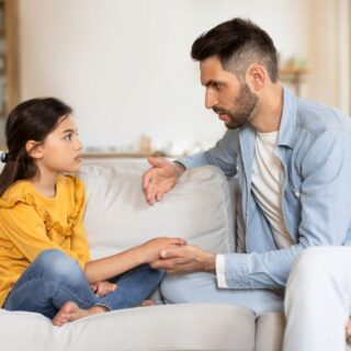 رجل يجلس على الأريكة ويمسك بيد بنت صغيرة تجلس بجانبه وينظر لوجهها
