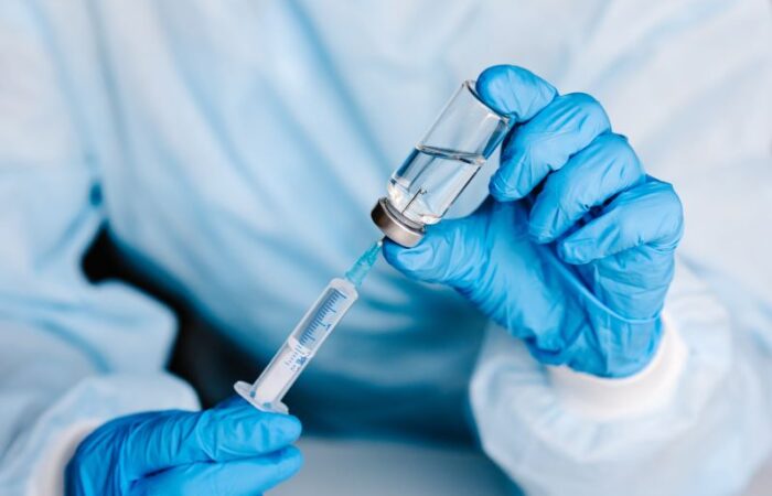 يدي طبيب يرتدي قفازات زرقاء ويقوم بسحب الدواء بواسطة إبرة من زجاجة صغيرة