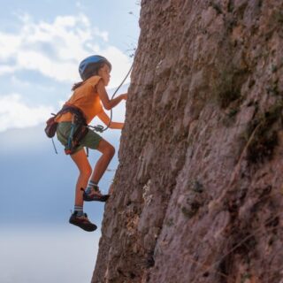 فتاة صغيرة تتسلق الجبل وترتدي المعدات الرياضية كخوذة الرأس