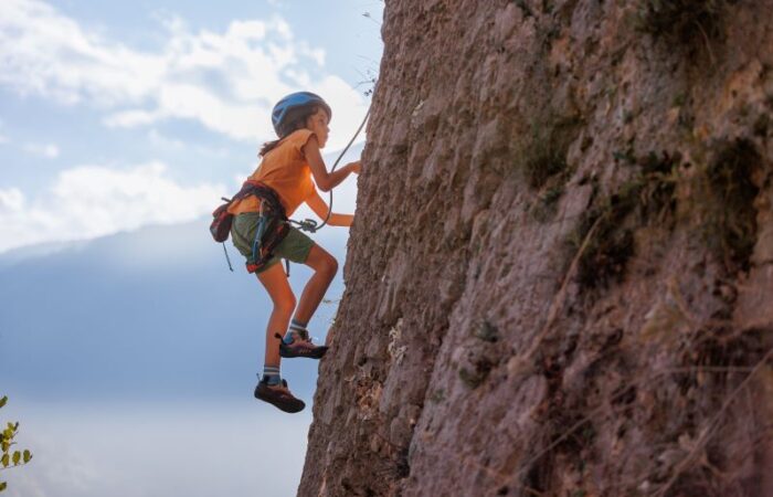 فتاة صغيرة تتسلق الجبل وترتدي المعدات الرياضية كخوذة الرأس