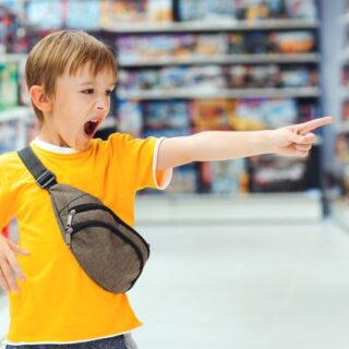 طفل يرتدي كنزة صفراء يقف في وسط المتجر وهو يصرخ ويشير بإصبعه للأمام