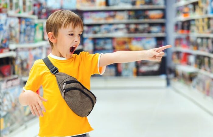 طفل يرتدي كنزة صفراء يقف في وسط المتجر وهو يصرخ ويشير بإصبعه للأمام