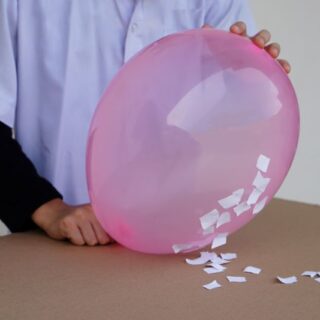 شخص يمسك بالون زهري اللون وعليه قصاصات ورقية