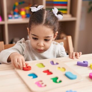 فتاة صغيرة تجلس على كرسي في المنزل وأمامها على الطاولة مكعبات أرقام ملونة