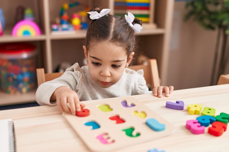 فتاة صغيرة تجلس على كرسي في المنزل وأمامها على الطاولة مكعبات أرقام ملونة