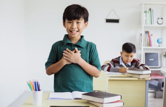 صبي يقف أمام طاولة في الصف ويضع يديه مضمومتين على صدره