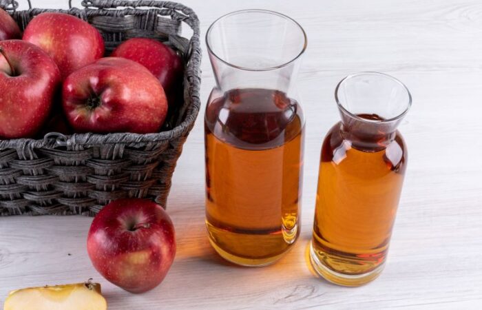 عبوات زجاجية تحتوي على سائل بني اللون وبجانيهم ثمرات التفاح