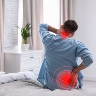 رجل بالغ يجلس على السرير ويضع يد على أسفل ظهره واليد الأخرى خلف رقبته