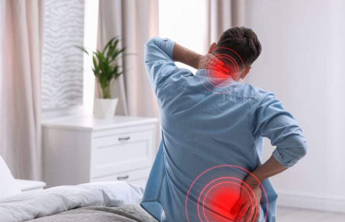 رجل بالغ يجلس على السرير ويضع يد على أسفل ظهره واليد الأخرى خلف رقبته