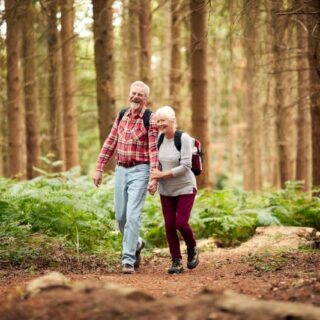 رجل مسن يمسك بيد امرأة مسنة يمشون ضمن الغابة