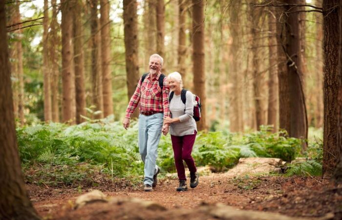 رجل مسن يمسك بيد امرأة مسنة يمشون ضمن الغابة