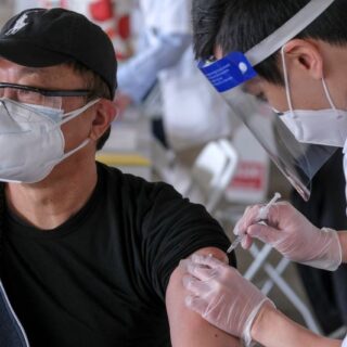 طبيب يرتدي قناع يقوم بإعطاء اللقاح لرجل بالغ