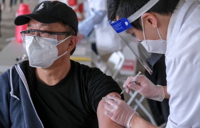 طبيب يرتدي قناع يقوم بإعطاء اللقاح لرجل بالغ