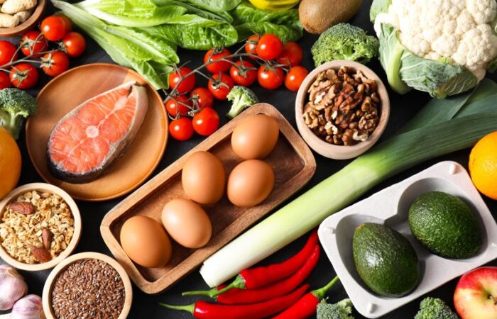 مجموعة من المأكولات: البيض، شرائح السمك، البروكلي، قرنبيط، الطماطم، فلفل حار، الأفوكادو، الجوز، اللوز، وأوراق الخس