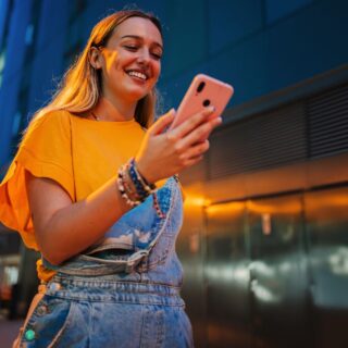 امرأة شابة مبتسمة وتمسك بيدها هاتف خليوي