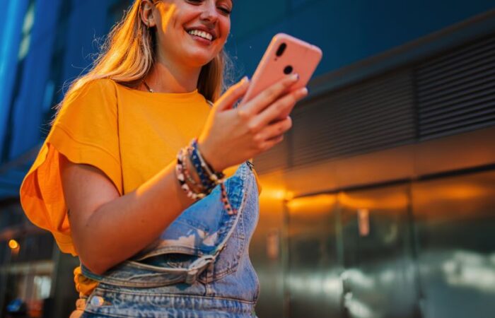 امرأة شابة مبتسمة وتمسك بيدها هاتف خليوي