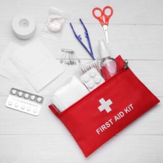 حقيبة صغيرة حمراء اللون مرسوم عليها إشارة + وبجانبها يوجد مقص وضماد طبي وظروف أدوية