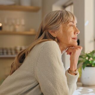 امرأة مسنة تبتسم وهي تضع يدها أسفل ذقنها وتنظر من النافذة