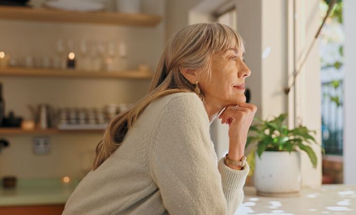 امرأة مسنة تبتسم وهي تضع يدها أسفل ذقنها وتنظر من النافذة