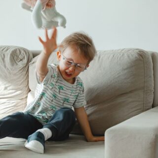 طفل يجلس على الأريكة وهو يصرخ ويرمي الدمية على الأرض