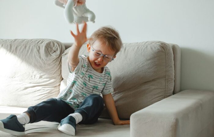 طفل يجلس على الأريكة وهو يصرخ ويرمي الدمية على الأرض