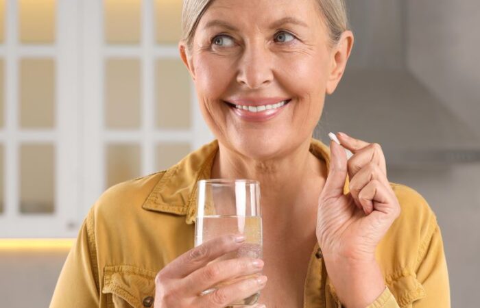 امرأة مسنة تمسك بيدها حبة دواء وباليد الأخرى كأس من الماء