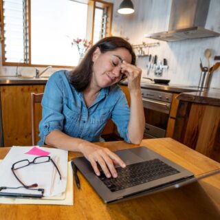 امرأة بالغة تجلس أمام مكتب في منزلها وتضع يدها على جبهتها