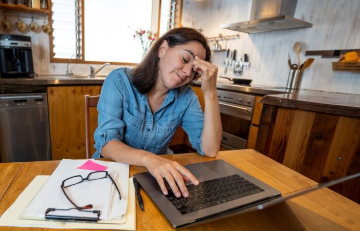 امرأة بالغة تجلس أمام مكتب في منزلها وتضع يدها على جبهتها